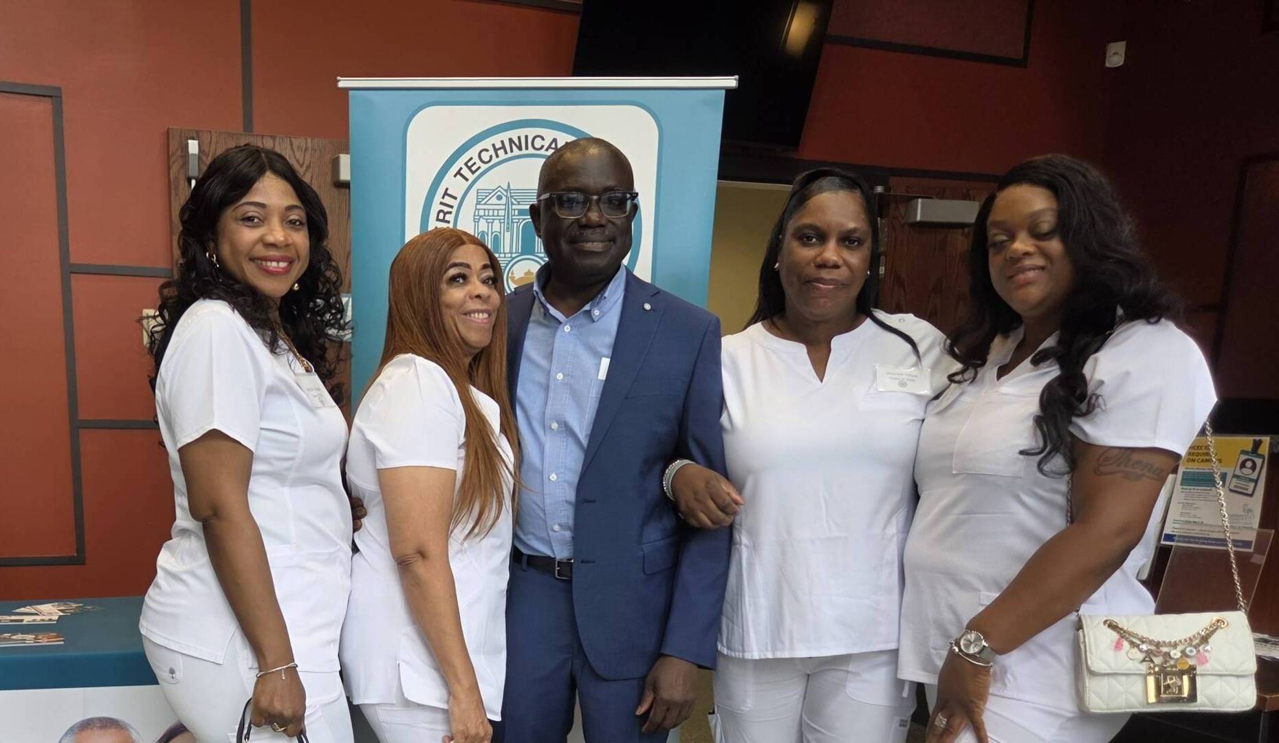 One man and four women stand together in front of a Merit Technical Institute LPN enrollment banner.